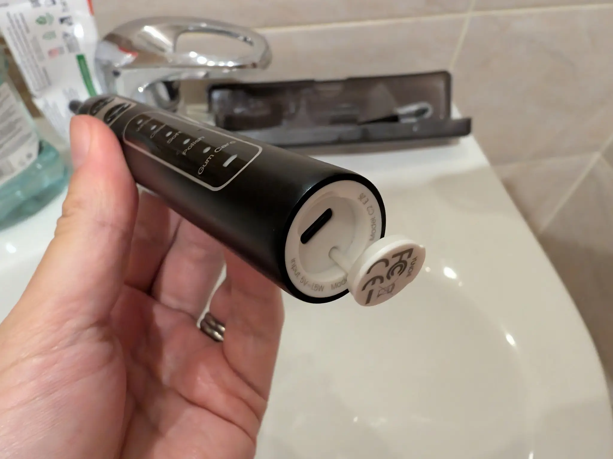 The bottom of an electric toothbrush. Under a flap is a USB-C port.